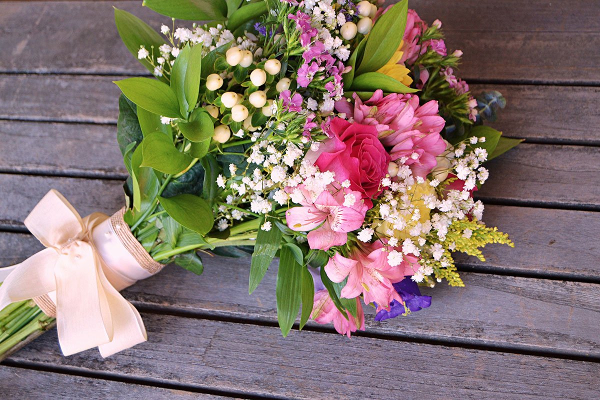 Ramo de flores coloridas con lazo de cinta crema sobre mesa de madera